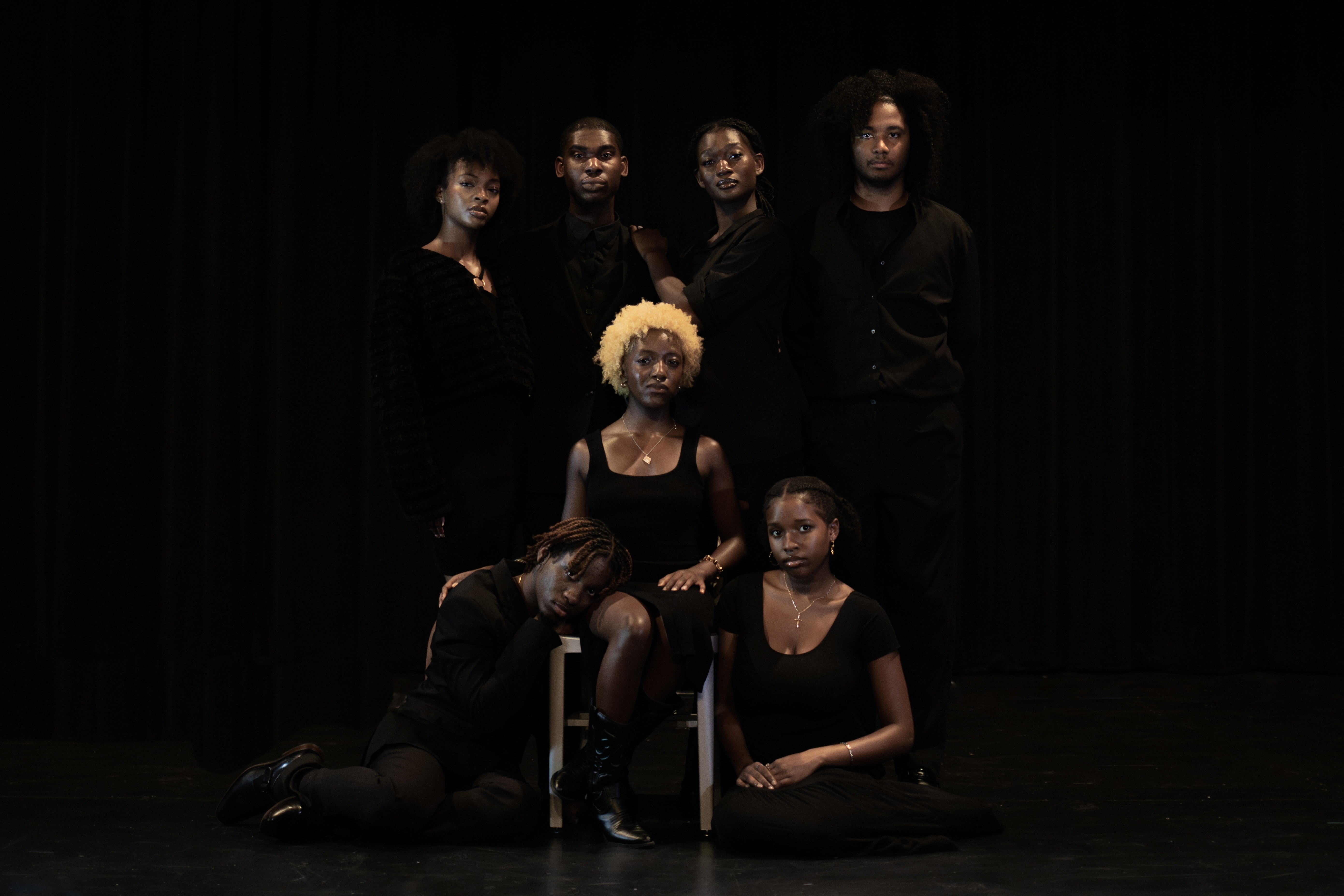 Amauriah seated with an ensemble cast on a dark stage