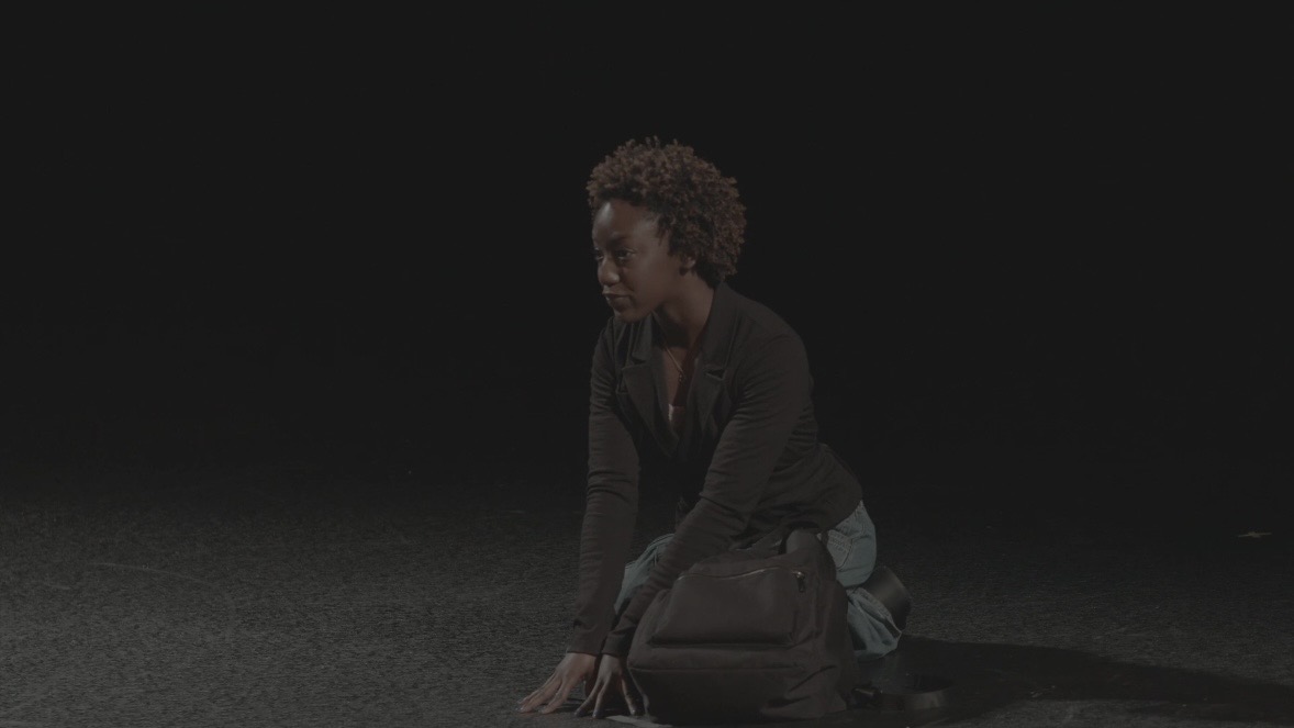 Amauriah kneeling on a dark stage